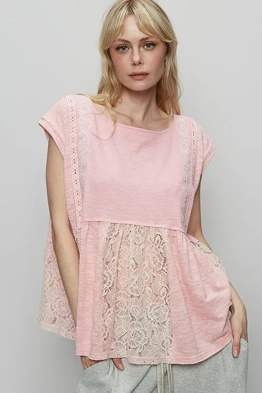 blonde woman standing in front of gray background with a sexy smile on her face wearing a light pink loose fitting empire waist embroidery and lace patchwork knit top with cap sleeves